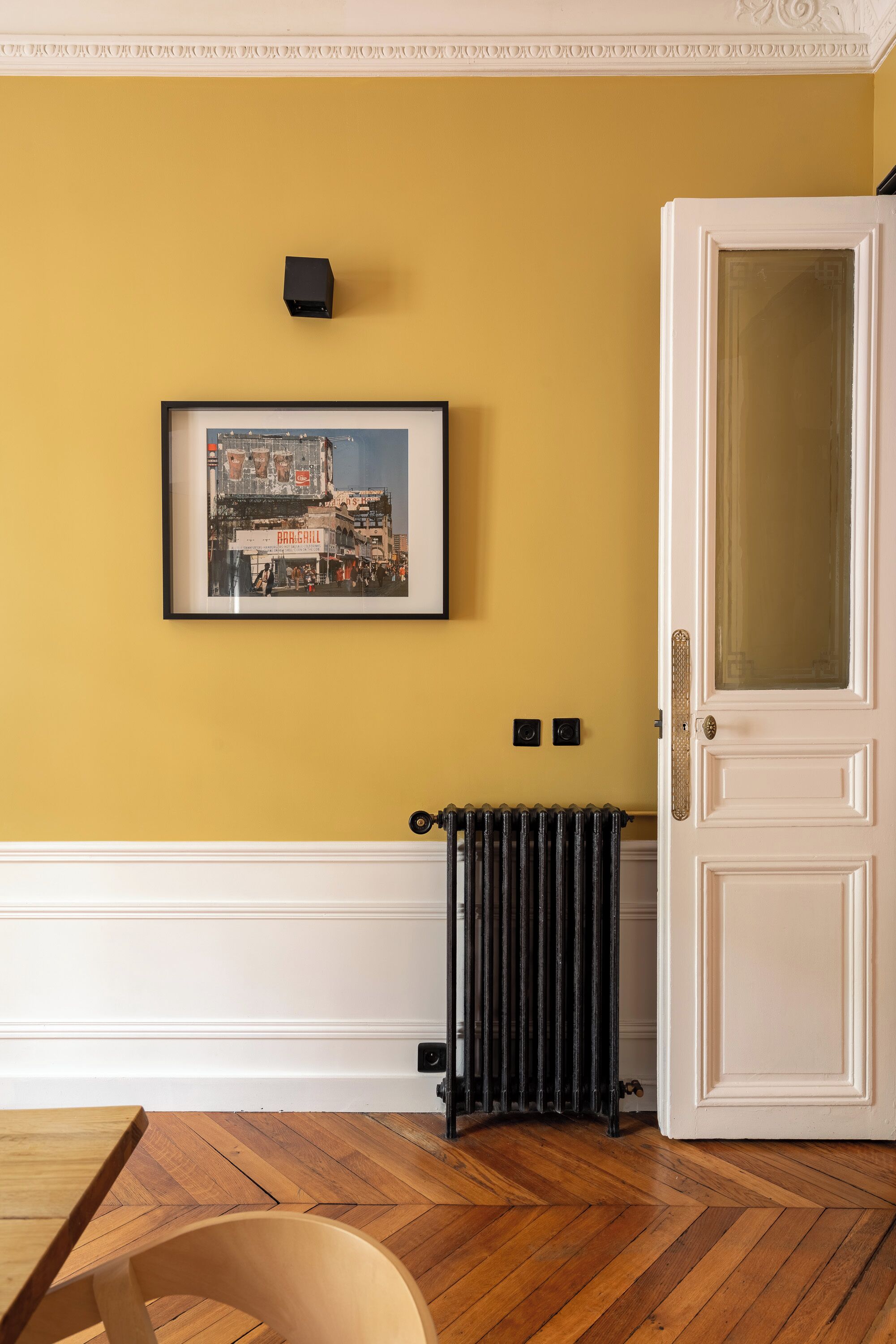 A room with a radiator, a framed cityscape picture, a white door, and a wooden floor.
