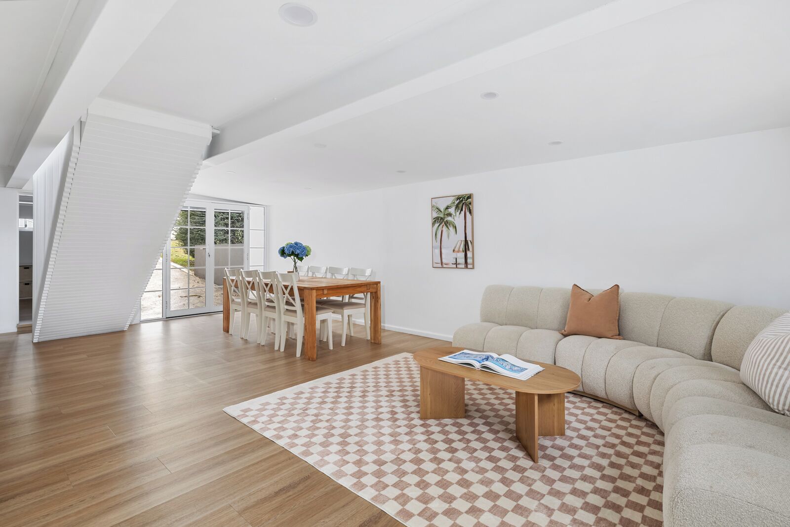 Ein modernes Wohnzimmer mit einem Holzesstisch, einem beigefarbenen Sofa und einem karierten Teppich.