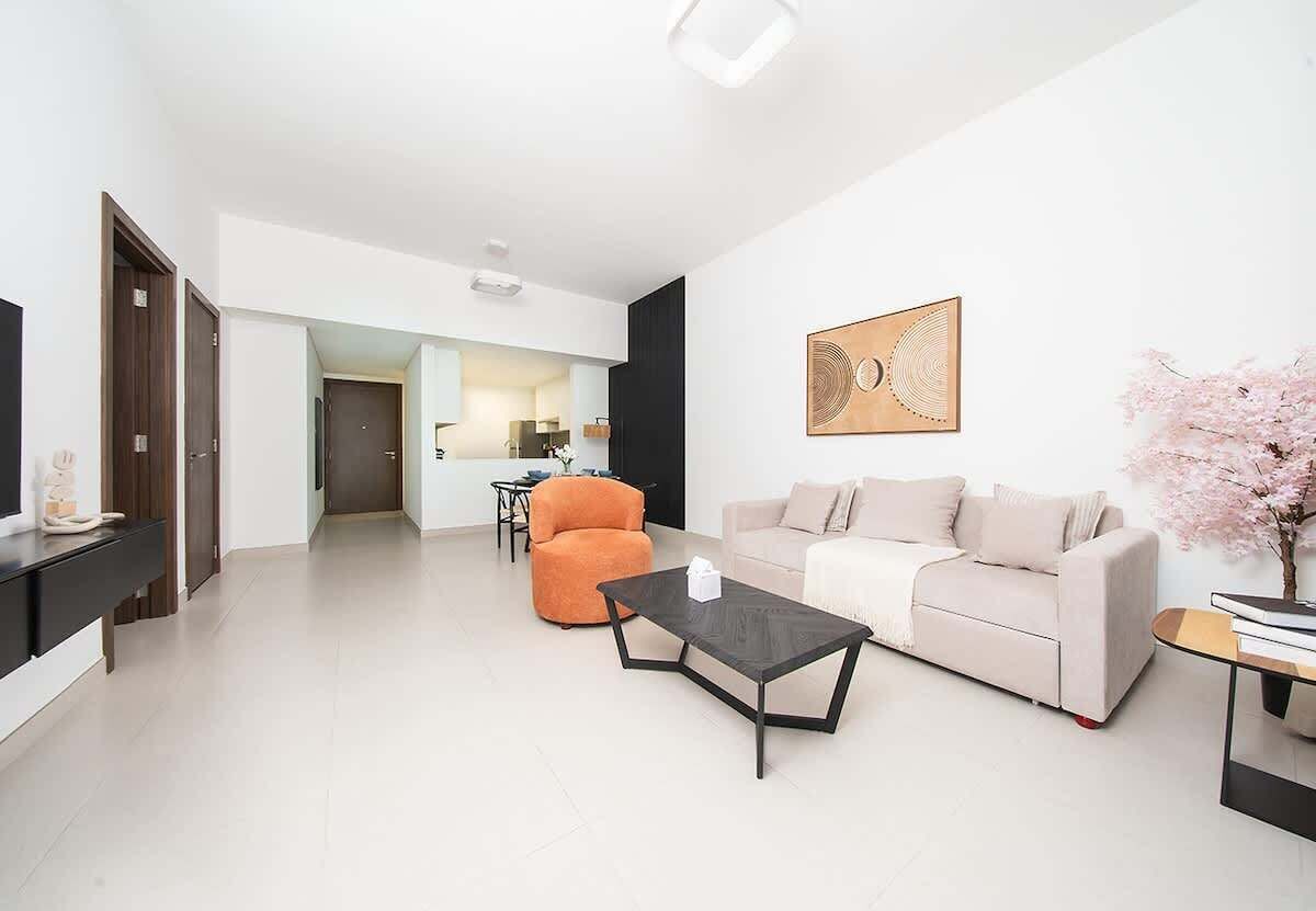 Een moderne woonkamer met een bank, een oranje fauteuil, een salontafel en een televisie.