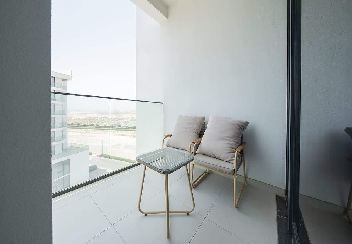 A balcony with a glass table and two cushioned chairs, overlooking a cityscape.