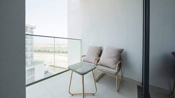 A balcony with a glass table and two cushioned chairs, overlooking a cityscape.