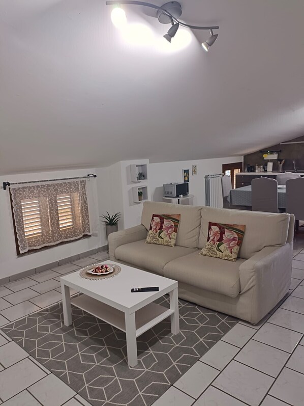 Una sala de estar con sofá, una mesa de centro, televisor y ventilador de techo.
