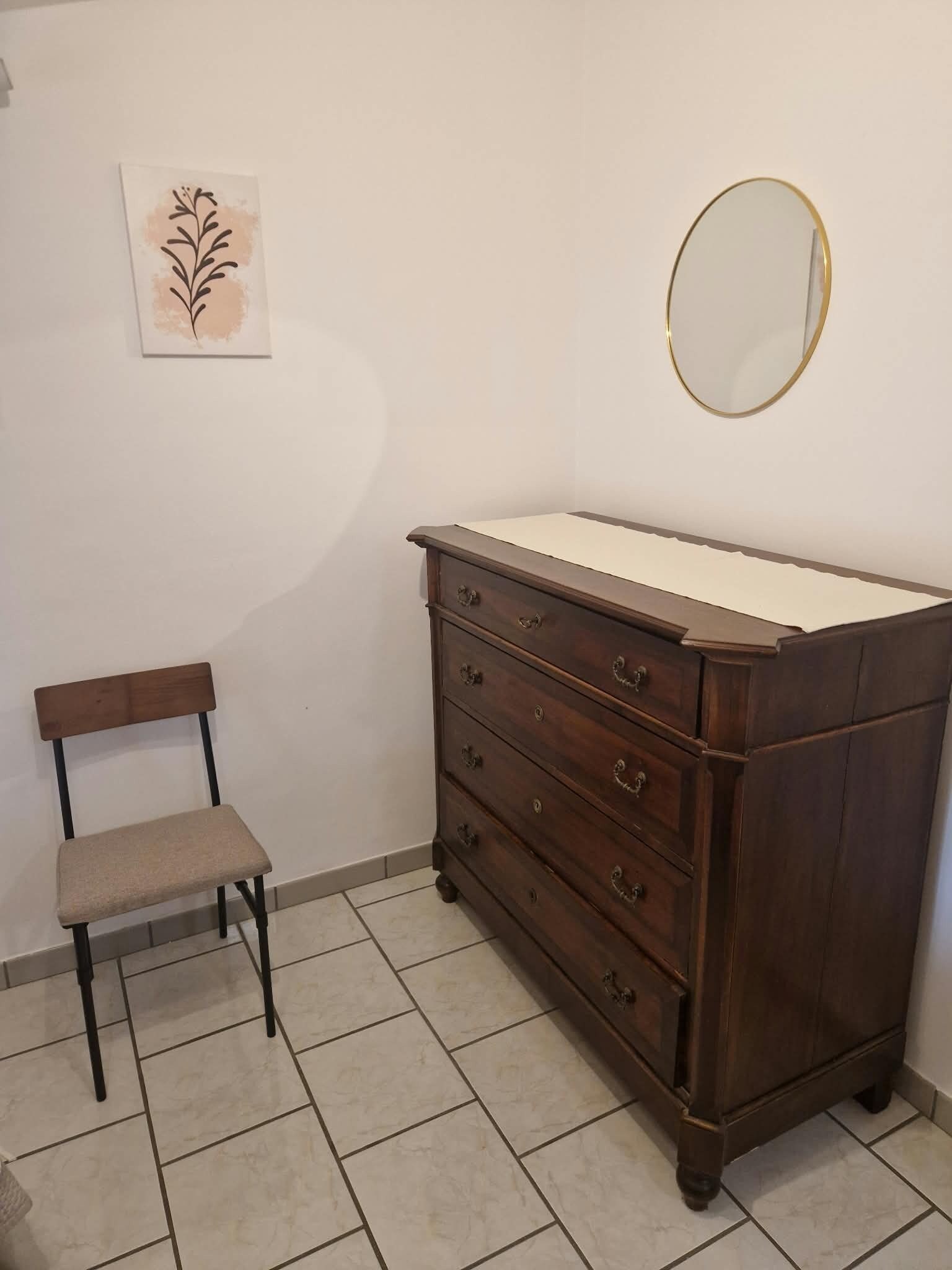 A room with a wooden dresser, a chair, a mirror, and a wall-mounted picture.