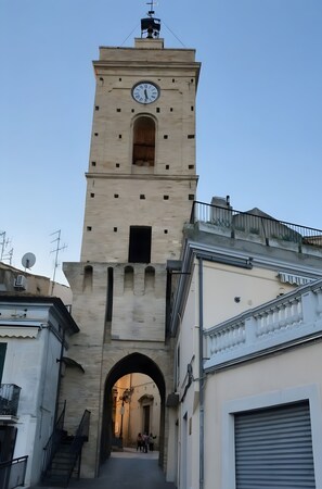 Ein hoher Turm mit einer Uhr, einem Bogenportal und einer Treppe, die zu ihm hinaufführt.