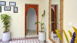 Um corredor com piso ladrilhado, porta de madeira, um espelho grande e diversas imagens emolduradas na parede.