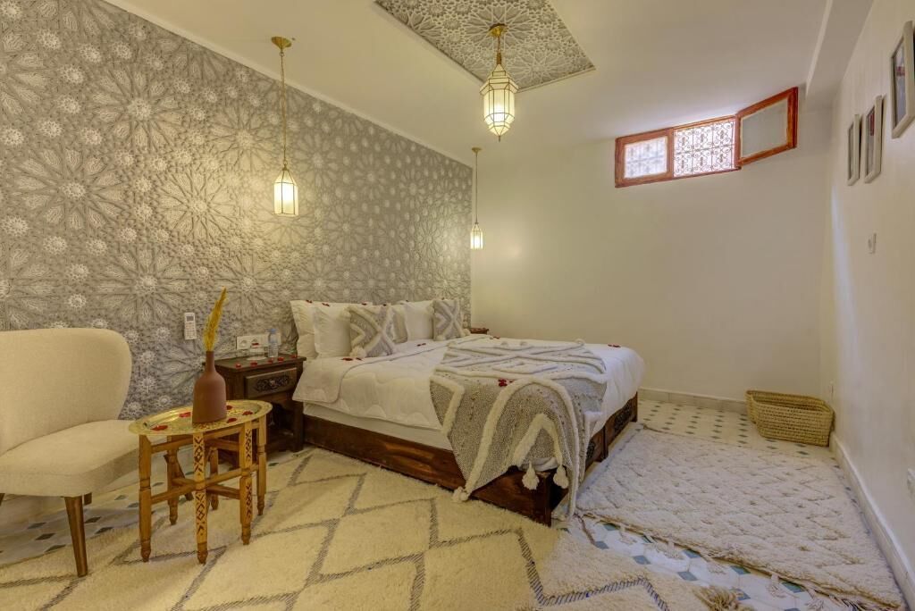 Un dormitorio con cama, mesita de noche, silla, pared decorativa y alfombra estampada.