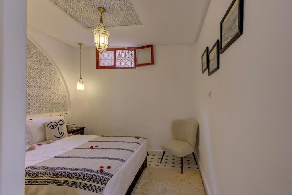 Un dormitorio con una cama, una silla, una mesita de noche, un estante en la pared y un techo con diseño.