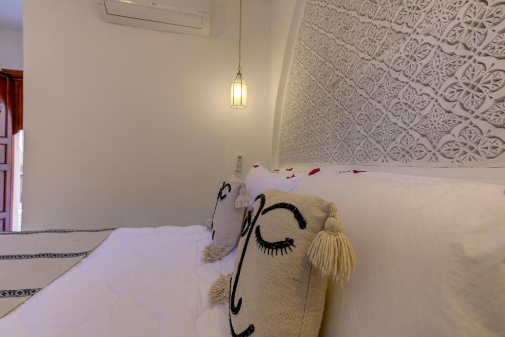 A bed with white bedding and decorative pillows, a patterned wall, and a hanging light fixture.