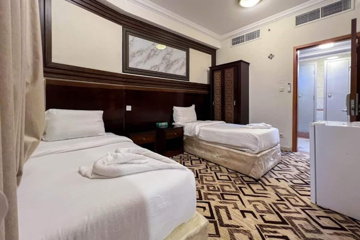 Ein Hotelzimmer mit zwei Betten, einem über den Betten hängenden Kunstwerk mit Marmorrahmen, einem Kleiderschrank und einem gemusterten Teppich.