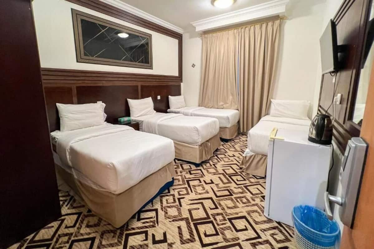 Ein Hotelzimmer mit zwei Betten, einer kleinen Küchenzeile, einem Fernseher und einem Fenster mit Vorhängen.