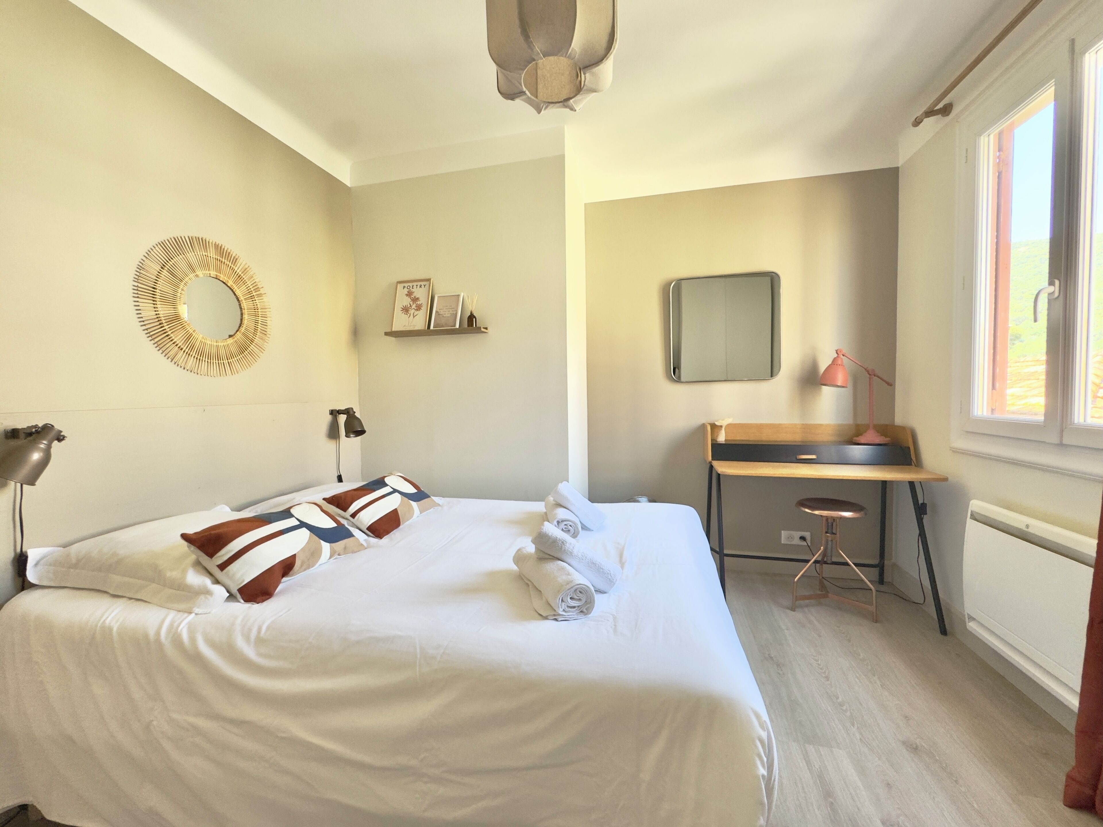 A hotel room with a bed, desk, chair, lamp, and a large window.