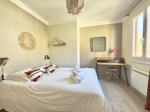 A hotel room with a bed, desk, chair, lamp, and a large window. - L'Ajax, 2-bedroom apartment in the city center and by the sea (Ajaccio)