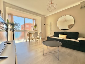 A modern living room with a sofa, a round mirror, a dining table with chairs, and a large window with curtains. - L'Ajax, 2-bedroom apartment in the city center and by the sea (Ajaccio)