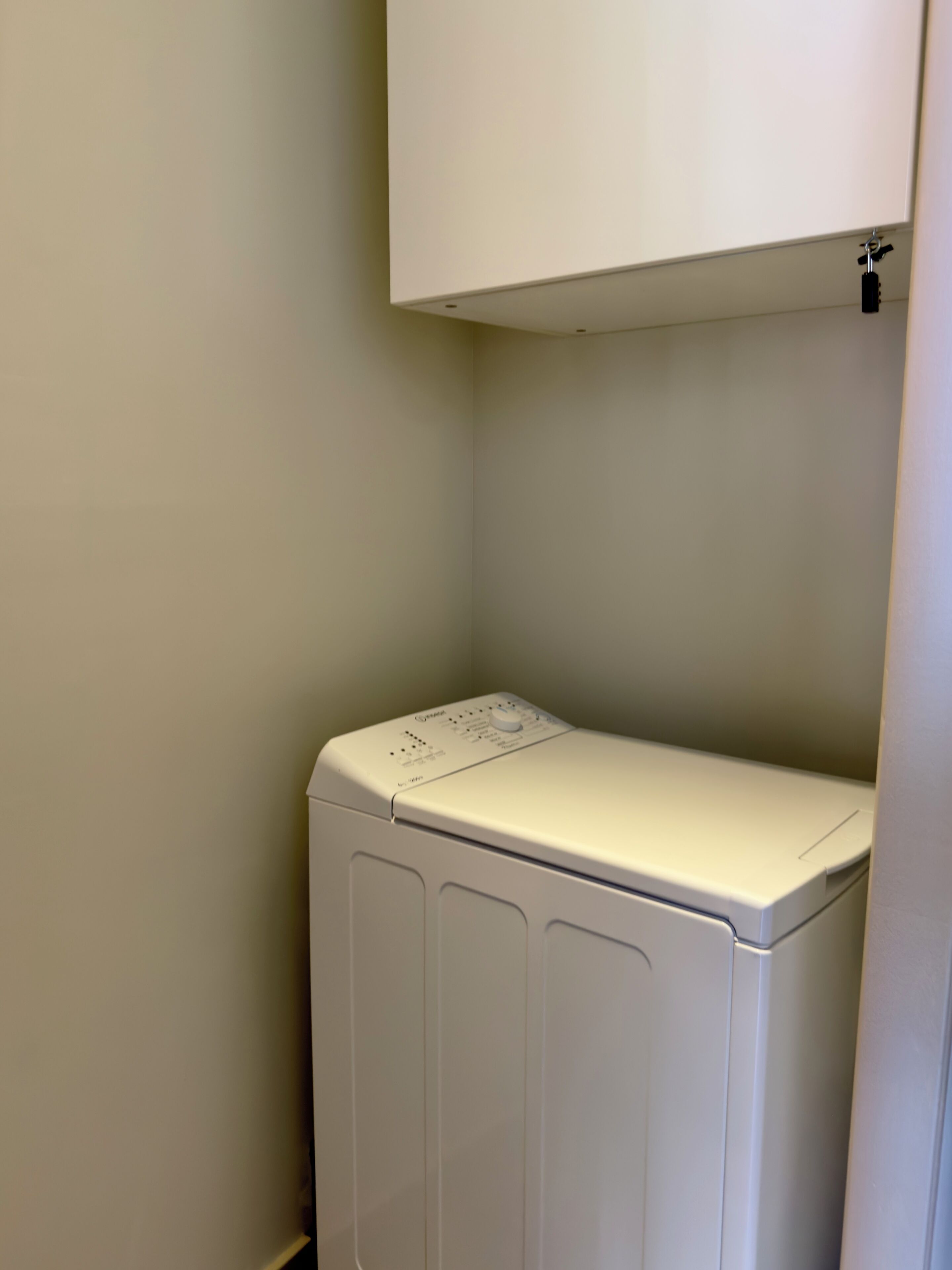 A compact, white, front-loading washer and dryer unit with a control panel on top, installed in a corner of a room with plain walls.