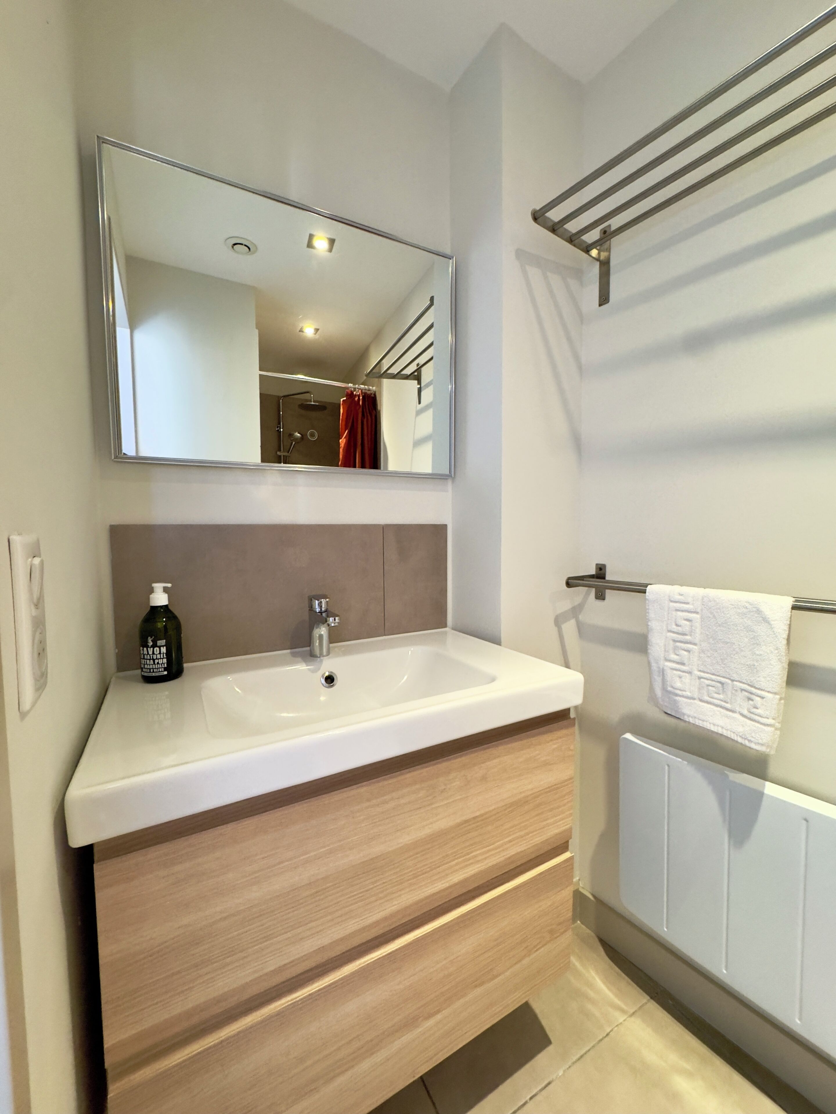 Une salle de bain moderne avec un lavabo blanc, un grand miroir, un porte-serviettes et un flacon de savon.