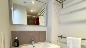 Ein modernes Badezimmer mit einem weißen Waschbecken, einem großen Spiegel, einem Handtuchhalter und einer Seife.