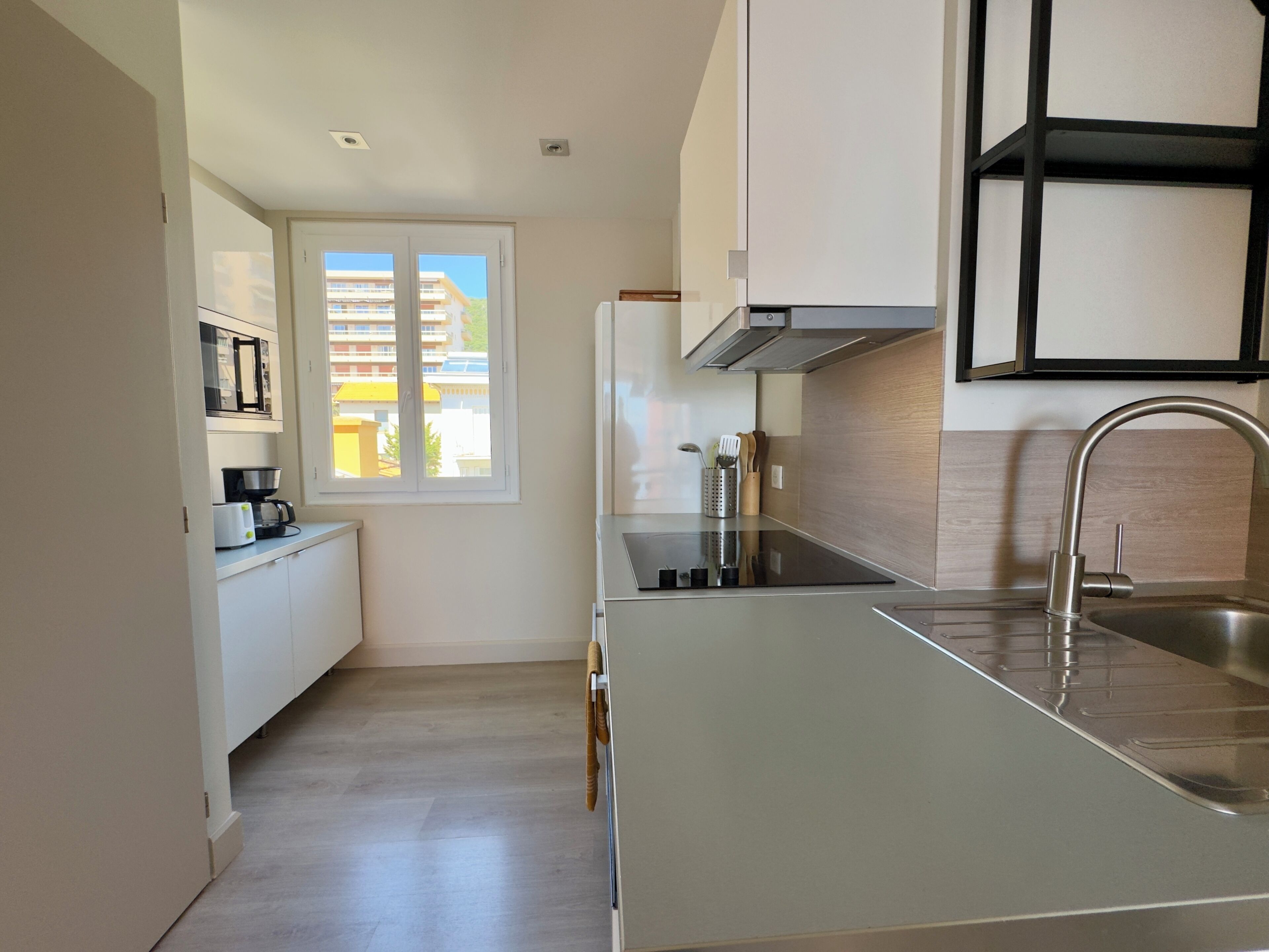 Een moderne keuken met een ingebouwde oven, een spoelbak en een raam met uitzicht op gebouwen.