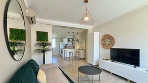 Ein modernes Wohnzimmer mit einer Couch, einem kleinen runden Tisch, einem Fernseher und einer Küche im Hintergrund.