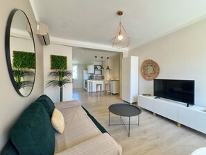 A modern living room with a sofa, a small round table, a TV, and a kitchen in the background. - L'Ajax, 2-bedroom apartment in the city center and by the sea (Ajaccio)