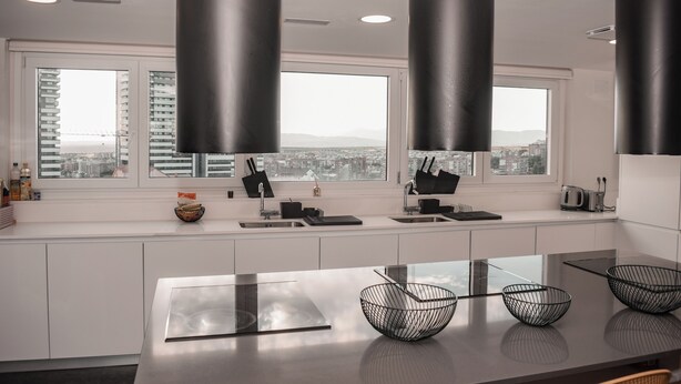 A modern kitchen with a large island, black pendant lights, and a city view through the windows.