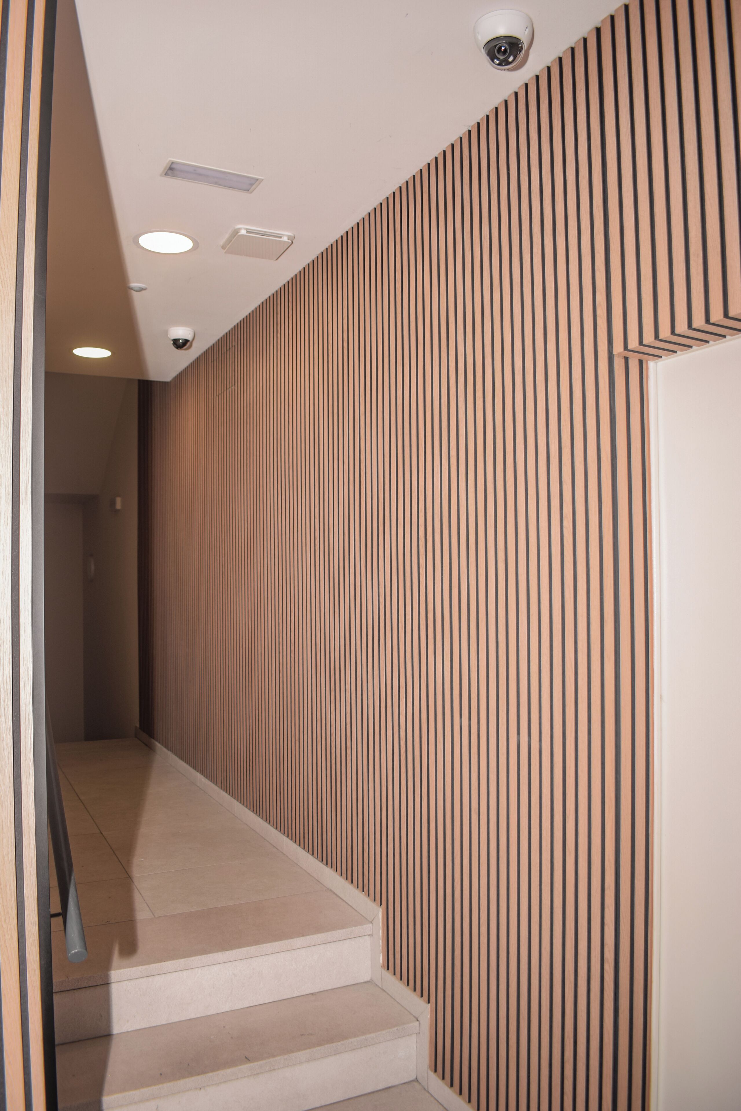 Un interior moderno con una escalera, paneles de madera e iluminación empotrada.