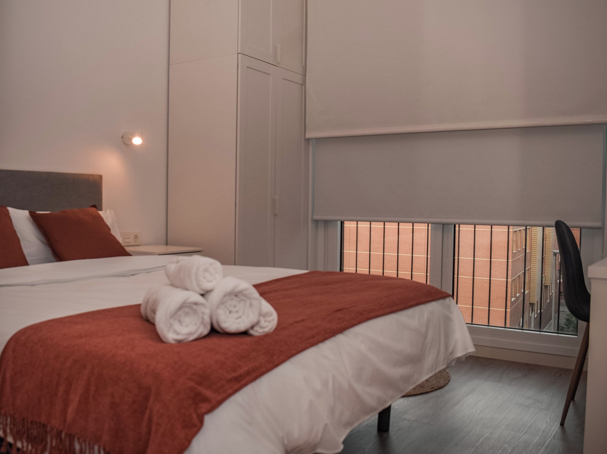 Hotellihuone, jossa on sänky, ikkuna, josta on näkymä rakennuksiin, yöpöytä ja tuoli.