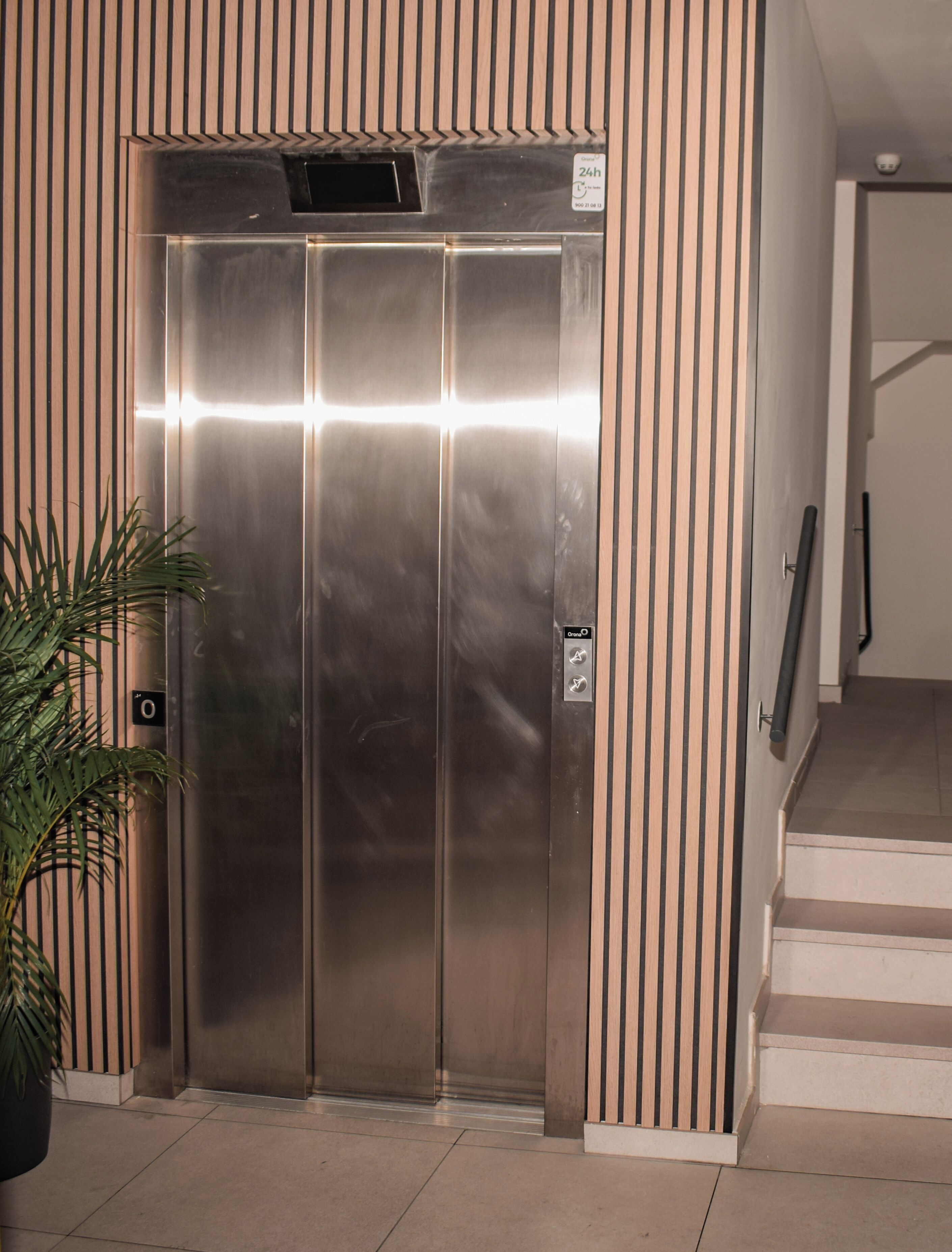 An elevator with a metallic finish, a control panel with a '0' button, and a stairway to the right.