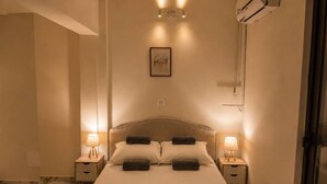 A hotel room with a bed, two bedside tables with lamps, a wall-mounted picture, and an air conditioning unit. - Elegant 2 Bedroom Apartment with Rooftop Terrace (Lemesos)