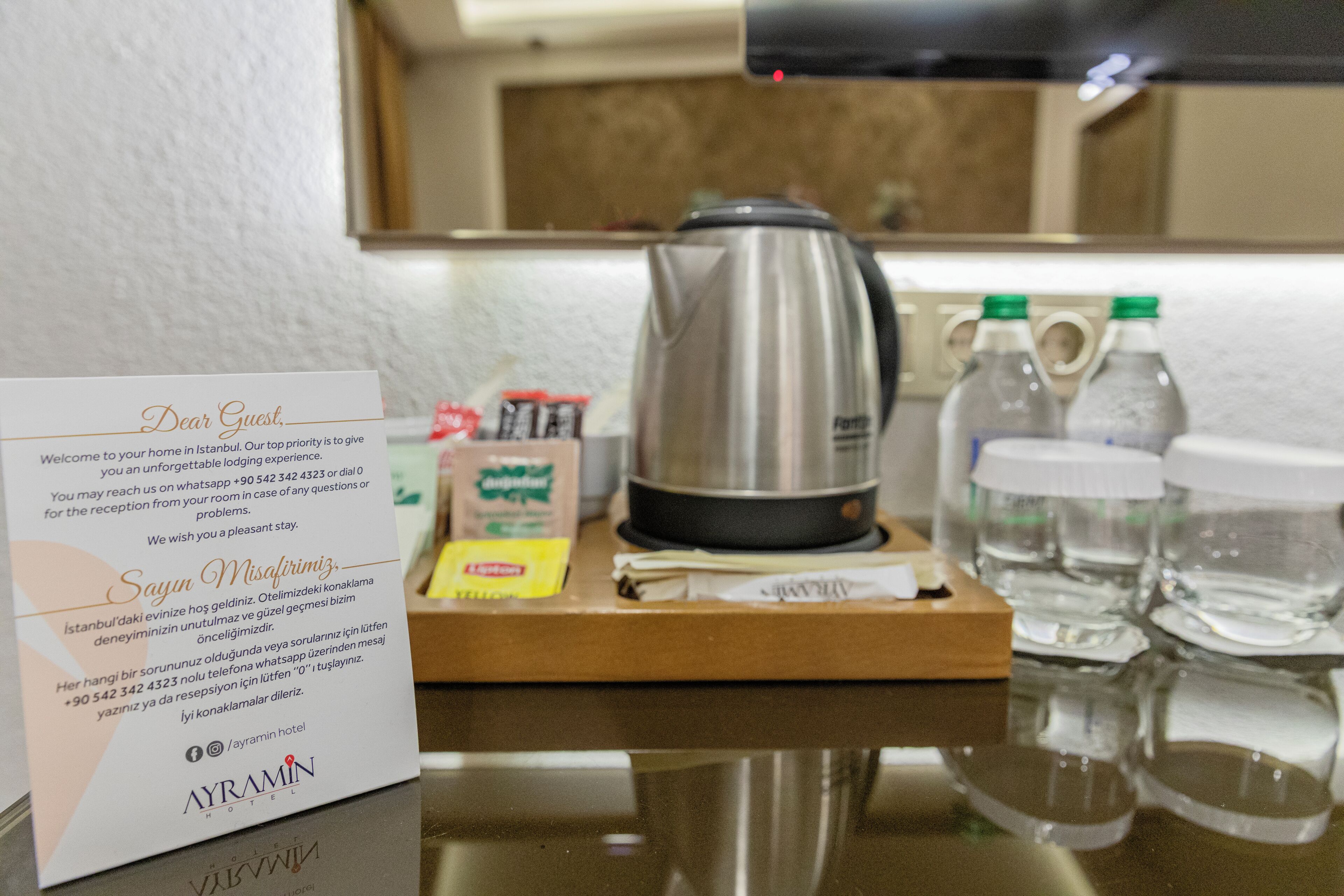 Ein Hotelrezeptionsbereich mit einer Willkommenskarte, einem Wasserkocher, Wasserflaschen und einer Kaffeemaschine auf der Theke.