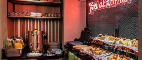 A breakfast buffet with various food items, a coffee machine, and a neon sign reading 'Feel at home'.