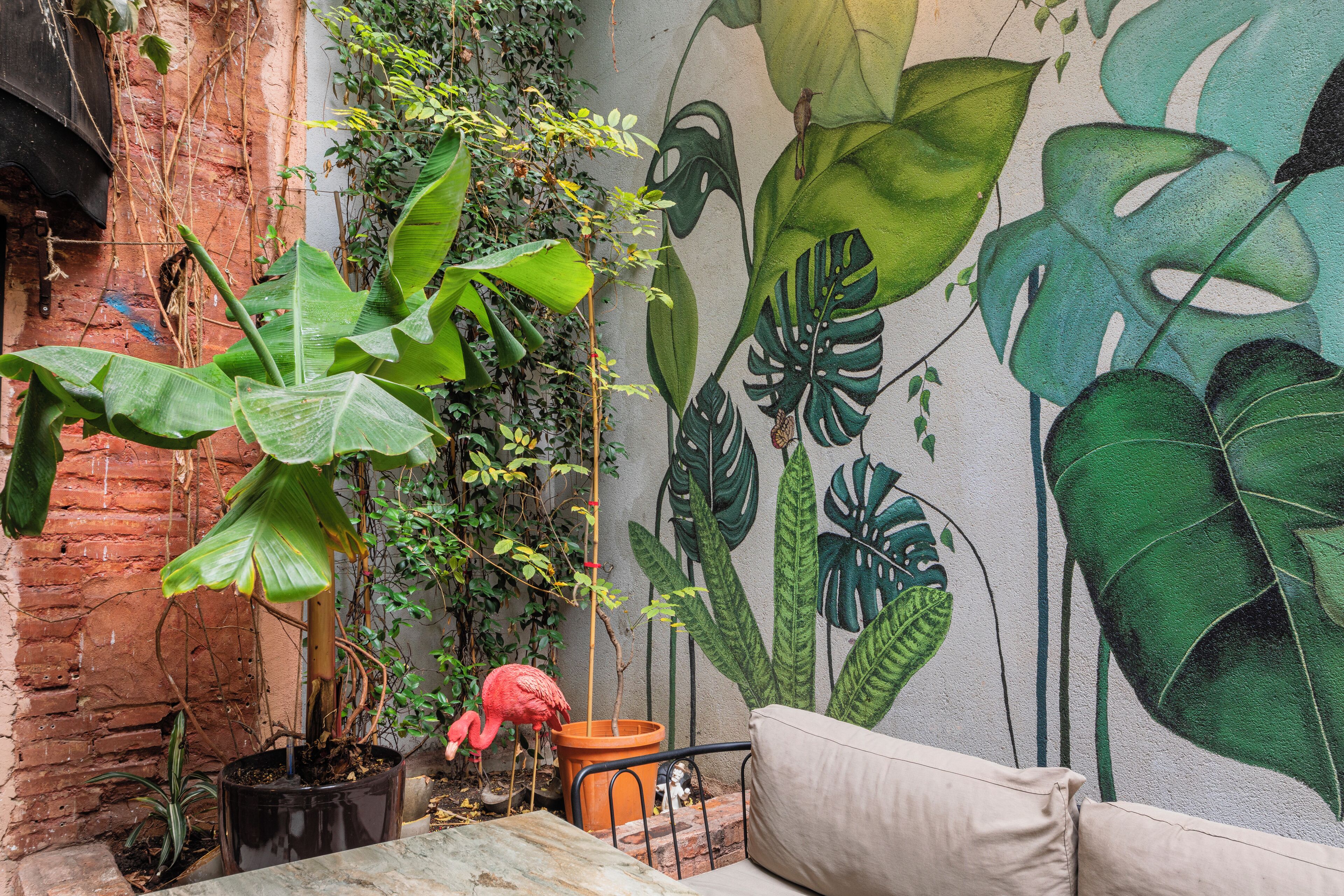 Una planta en maceta, una estatua de flamenco y un mural de hojas tropicales.