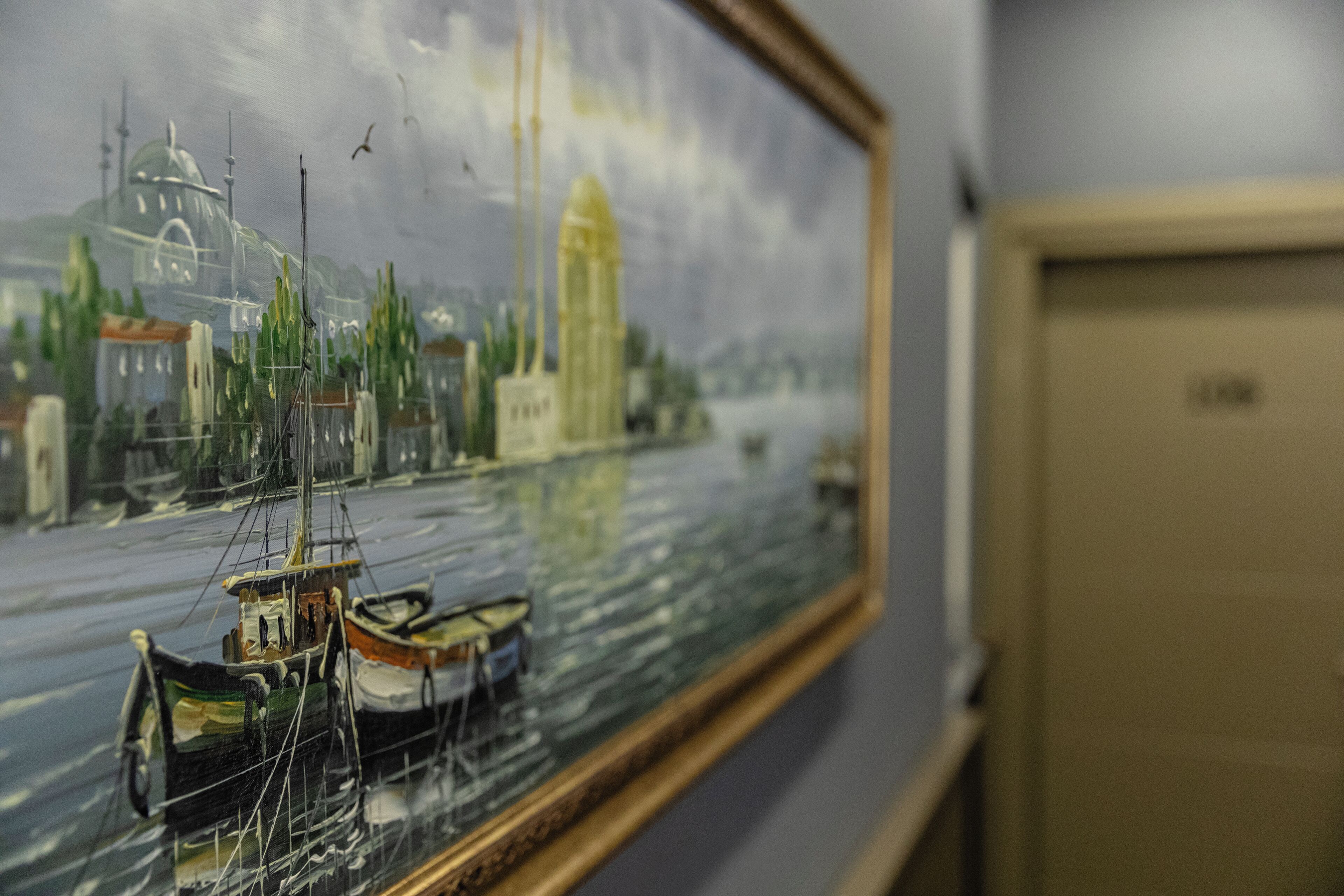 A framed painting of a harbor scene with boats and buildings.