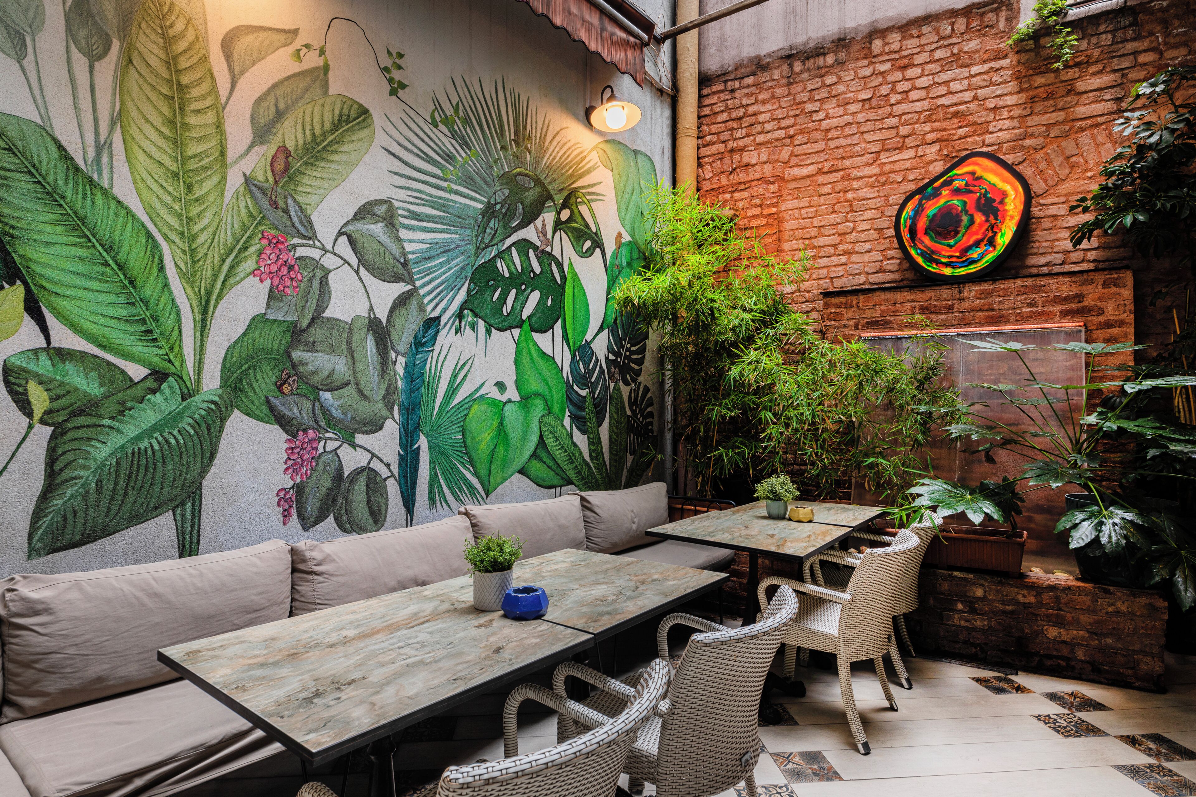 A patio with a mural, seating, tables, and potted plants.