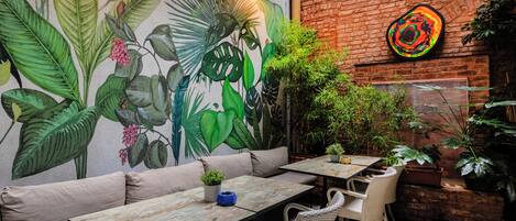 A patio with a mural, seating, tables, and potted plants.