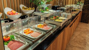 Un bufé con diversas opciones de comida, entre ellas frutas, verduras y carnes, presentadas en recipientes transparentes.