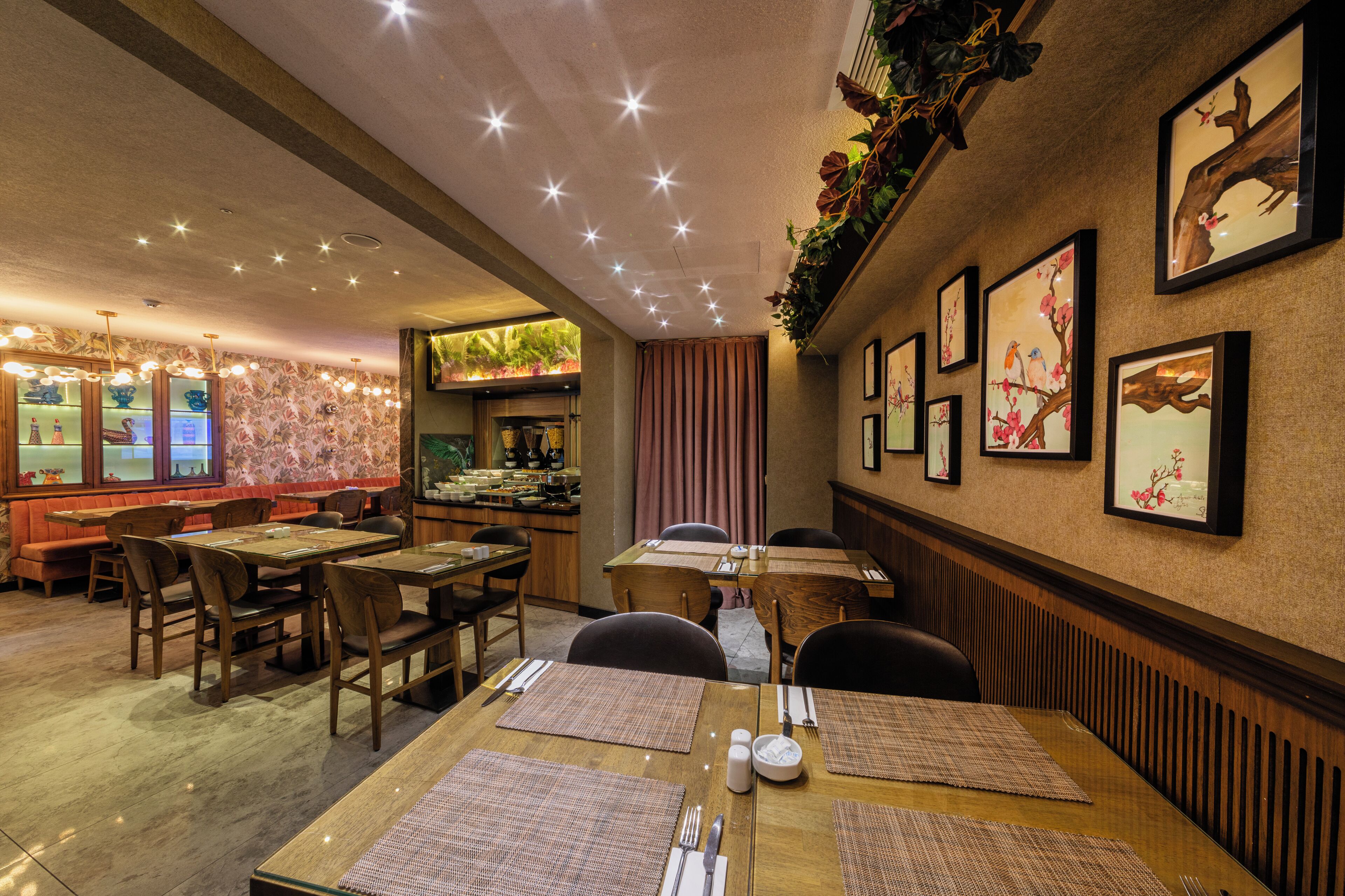 A restaurant with wooden tables and chairs, framed artwork on the walls, and a ceiling with star-like lights.