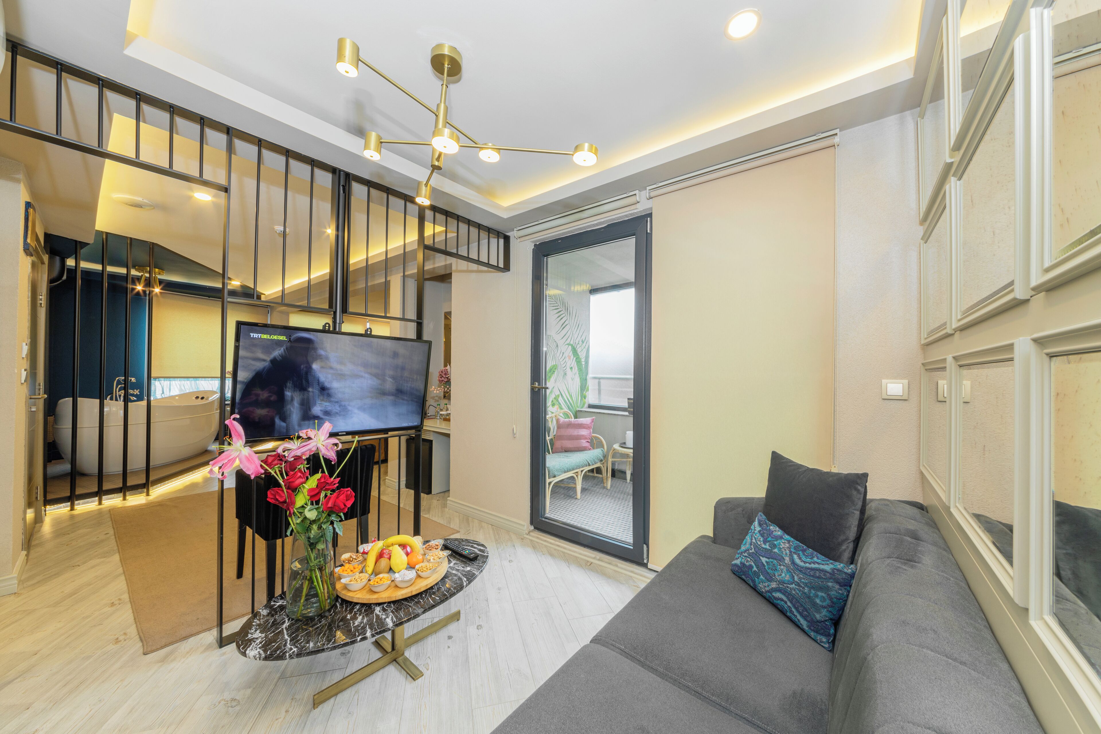 A modern living room with a sofa, a TV, a dining table with fruit, and a staircase.
