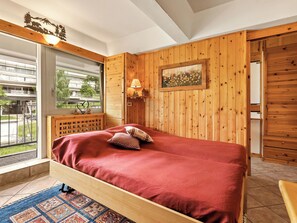 Ein Schlafzimmer mit einem Holzbett, einem Fenster mit Blick nach draußen, einer Lampe und einem gerahmten Bild an der Wand.