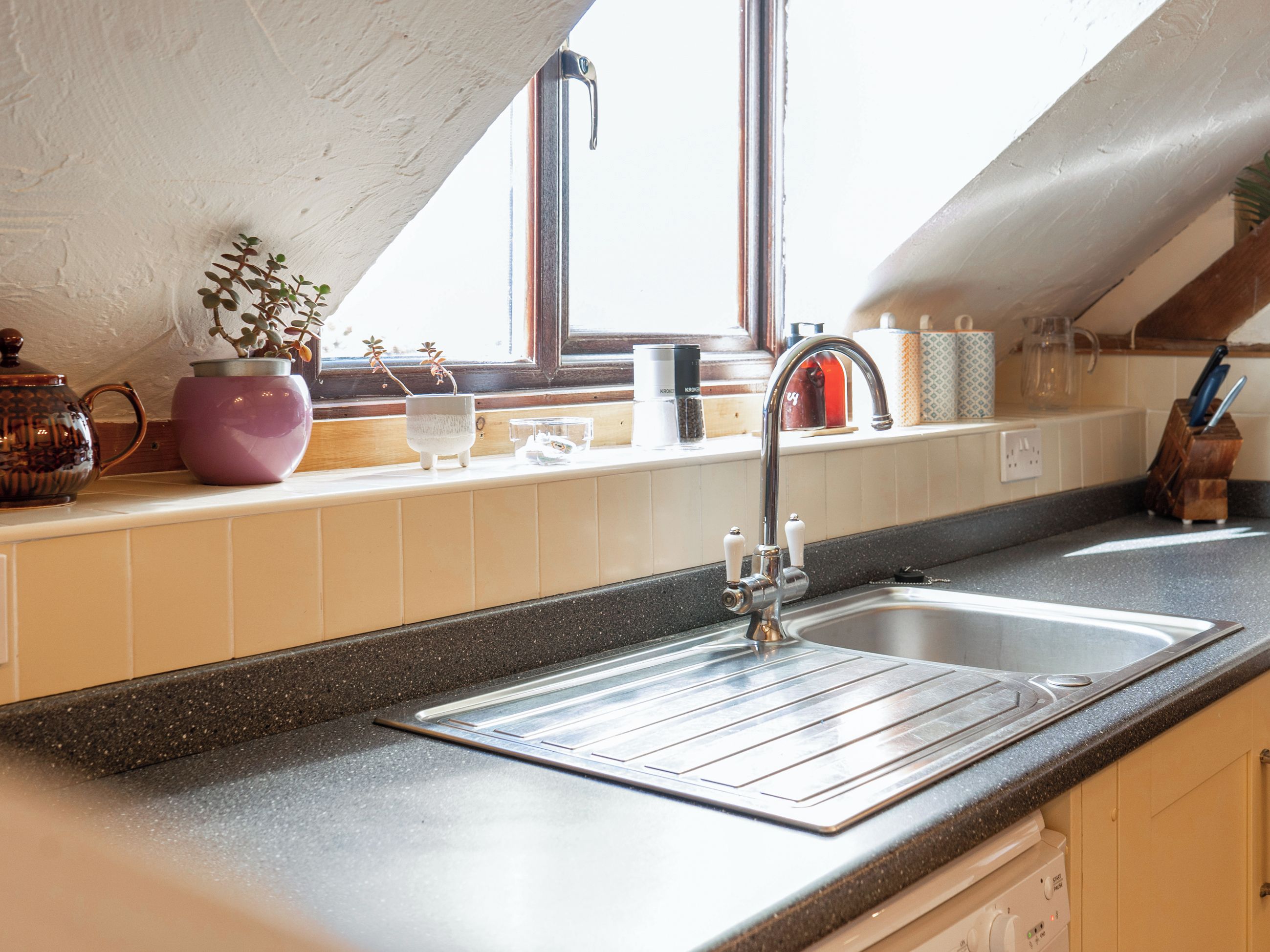 A kitchen with a stainless steel sink, a window above the counter, and various kitchen items on the windowsill.