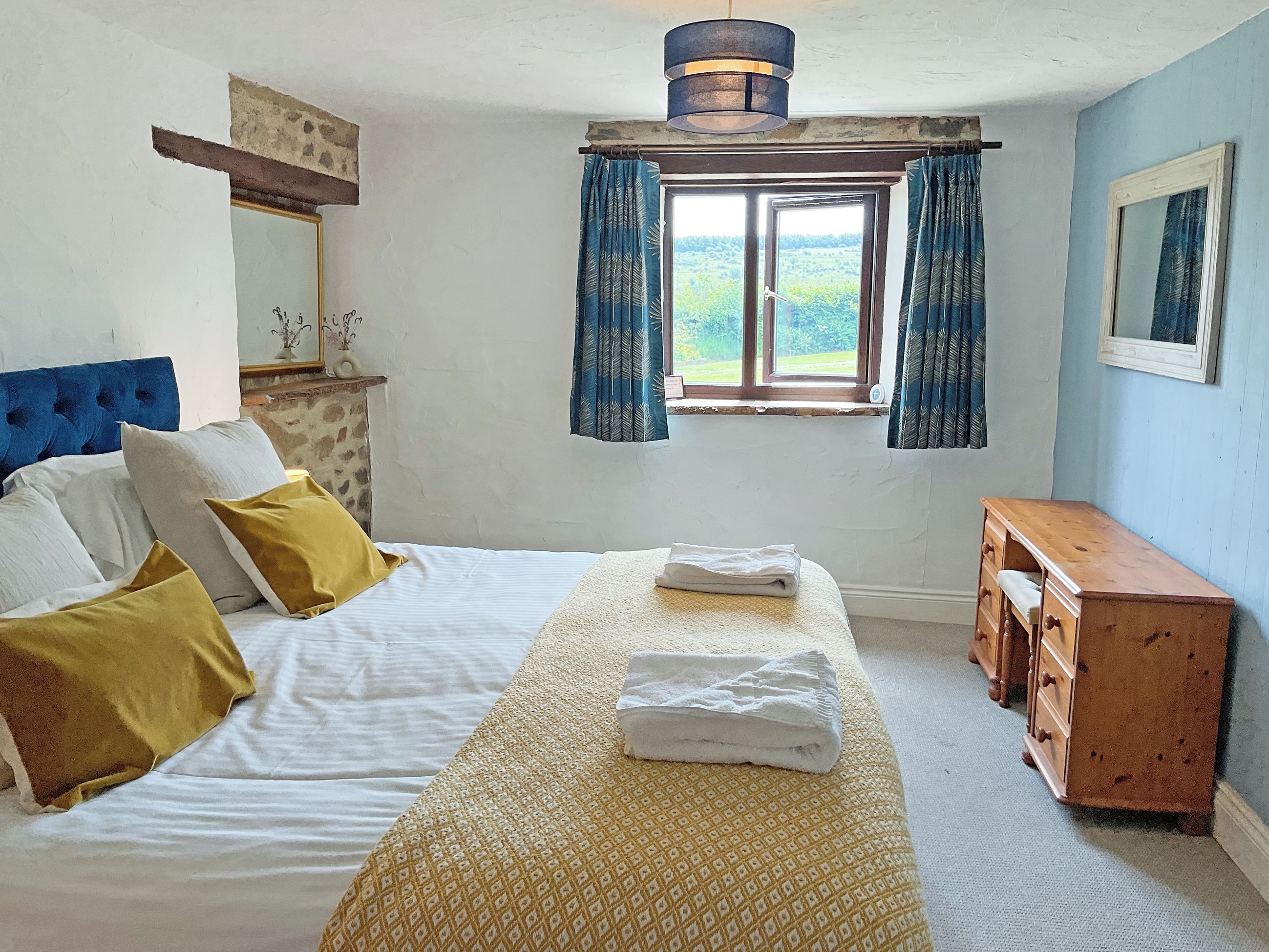 A bedroom with a bed, a wooden dresser, a window with curtains, and a view of greenery outside.