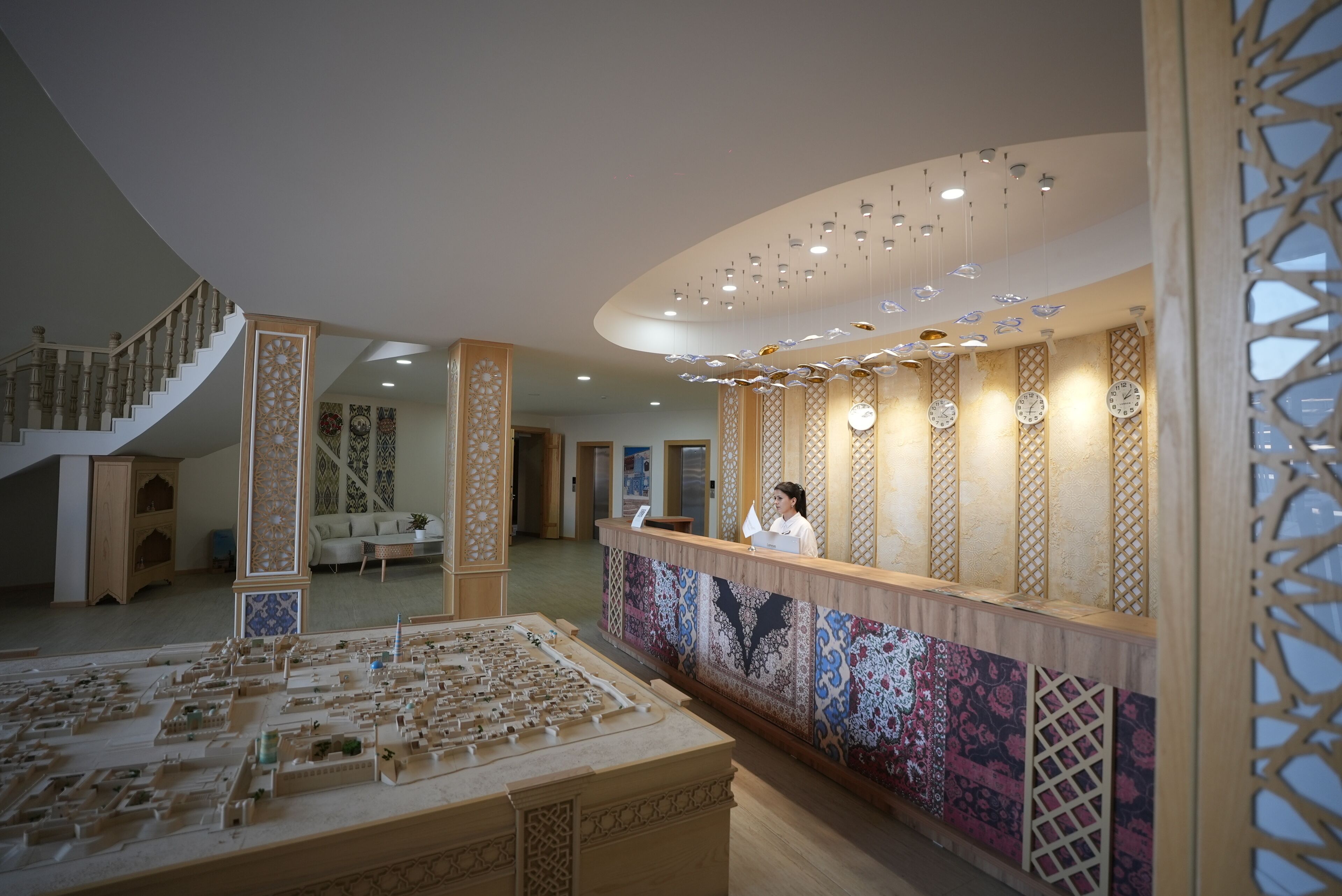 Vestíbulo de hotel con mostrador de recepción, una escalera y una maqueta urbana.