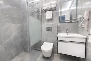 A modern bathroom with a glass-enclosed shower, a white toilet, and a sink with a mirror above it. - Lond Hotel (Beyoğlu)