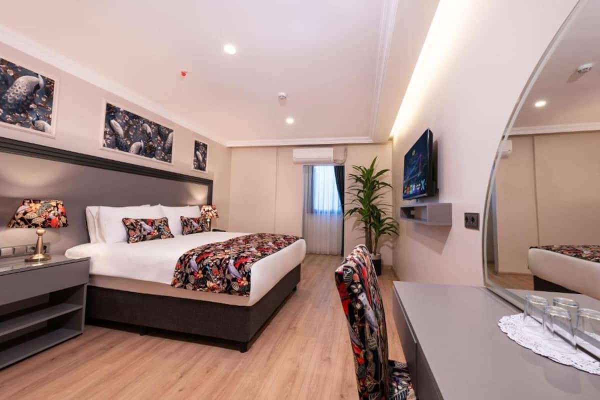 A modern hotel room with a bed, bedside table, mirror, and a TV.