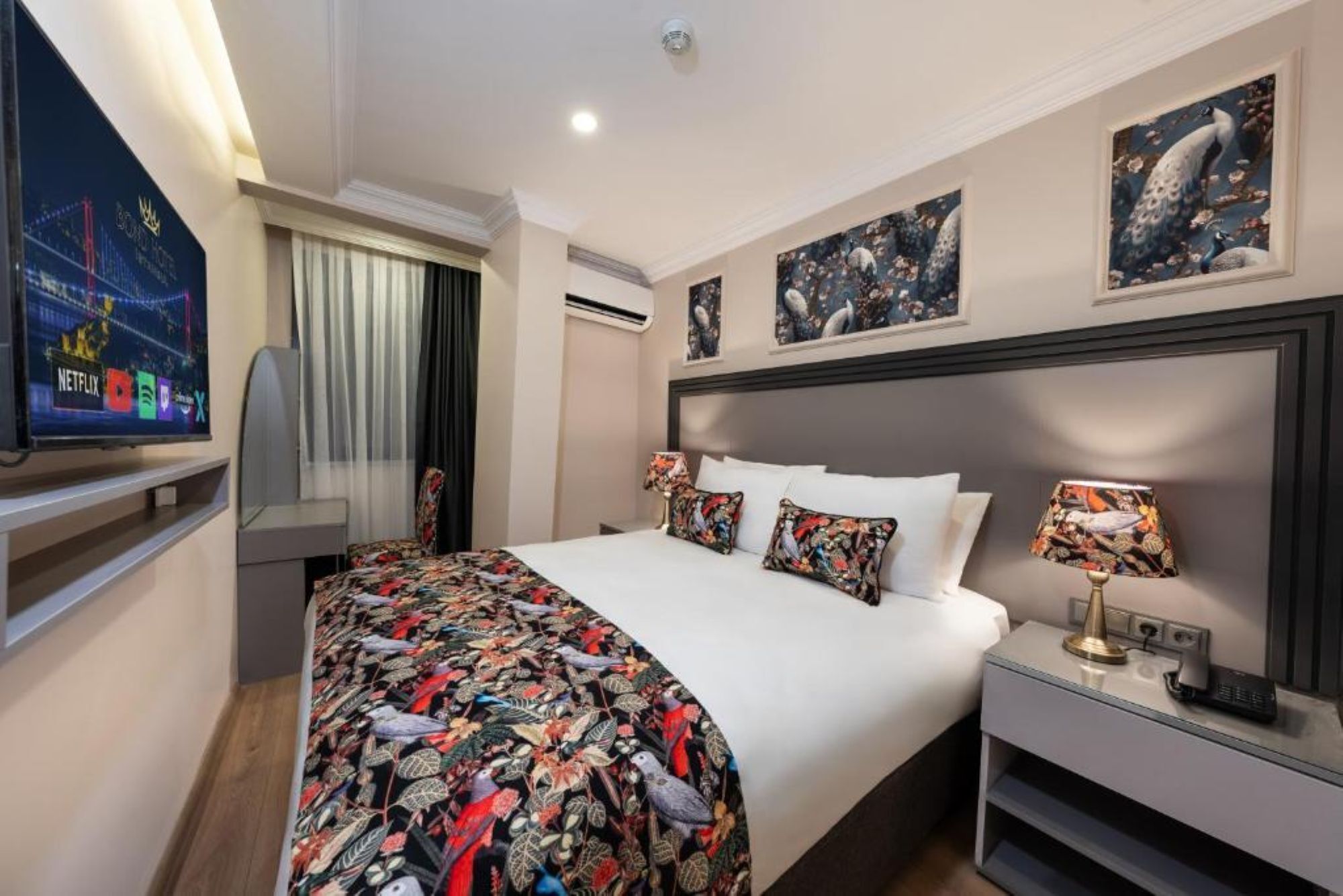A hotel room with a bed, a TV, a nightstand, and artwork on the walls.