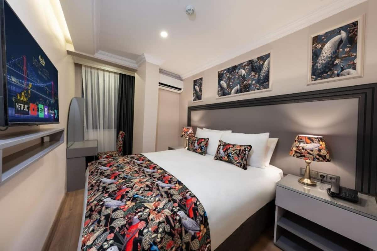 A hotel room with a bed, a TV, a nightstand, and artwork on the walls.
