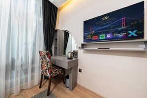 Ein Hotelzimmer mit einem Bett, einem Schreibtisch, einem Stuhl, einem an der Wand befestigten Fernseher und einem Fenster mit Vorhängen.