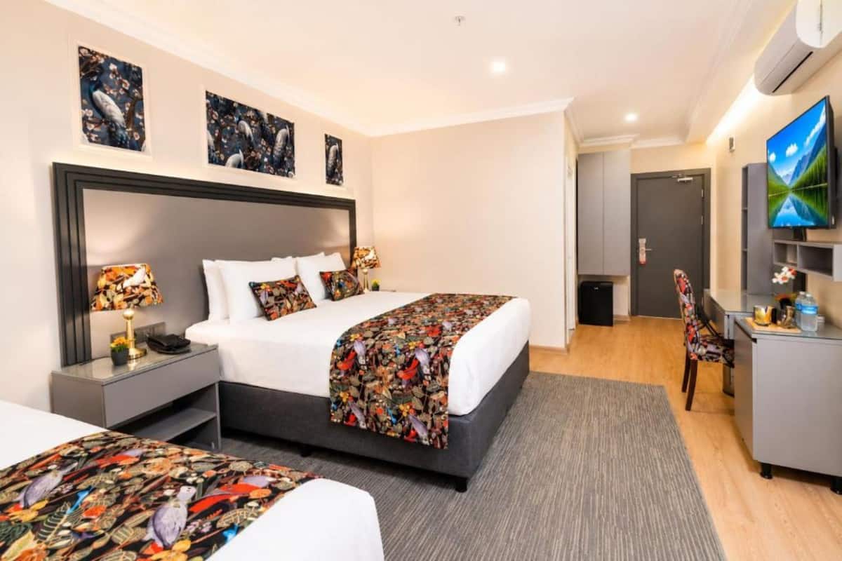 A hotel room with a bed, bedside tables, a desk, a chair, a TV, and artwork on the walls.