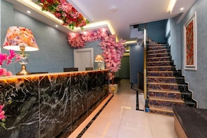 A reception desk with a marble counter, a staircase with patterned steps, and a decorative floral arrangement. - Lond Hotel (Istanbul)