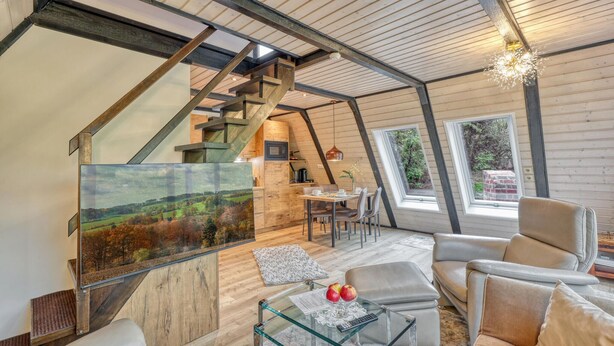 A loft-style room with a wooden ceiling, a dining area, and a large window with a view of trees.