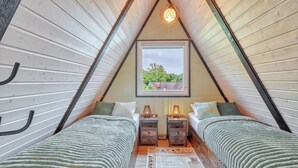 A triangular attic bedroom with two beds, a window with a view, and a unique spherical light fixture.